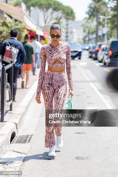 Cindy Bruna wears cropped wrapped top, high waisted pants, turquoise bag, sneaker, sunglasses during the 76th Cannes film festival on May 22, 2023 in...