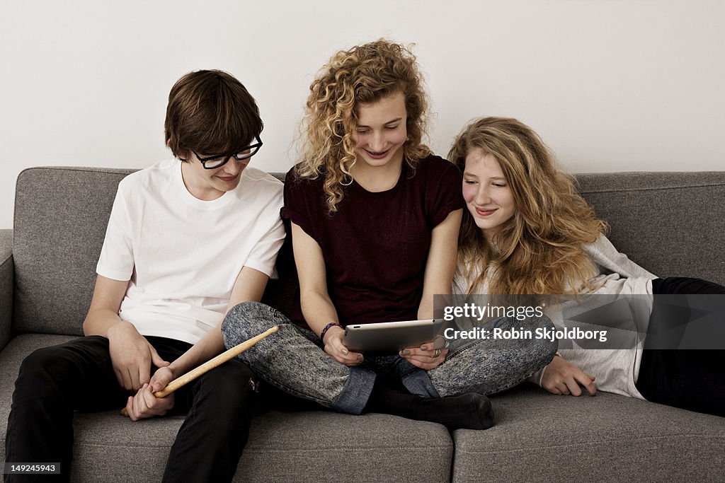 Teenagers sitting on sofa with drumsticks and tablet computer