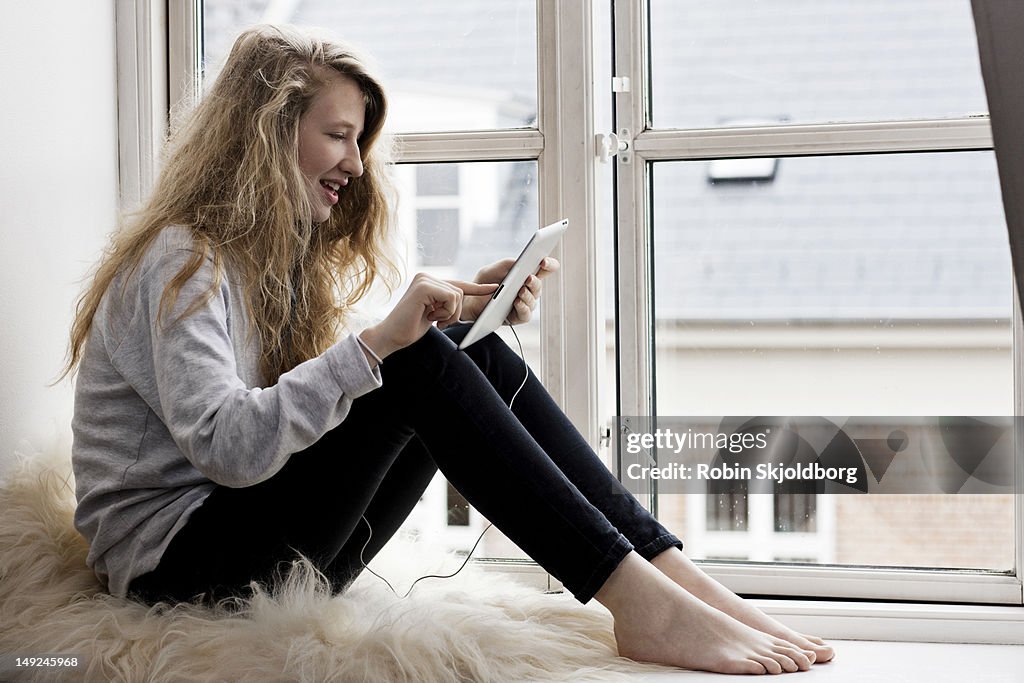 Girl sitting on window sill with tablet computer