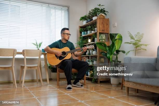 asiatischer mann mittleren alters, der zu hause gitarre spielt - handsome middle eastern men stock-fotos und bilder