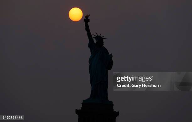 The sun is shrouded as it sets behind the Statue of Liberty in a hazy sky caused by smoke drifting into the Northeast of the U.S. From wildfires in...