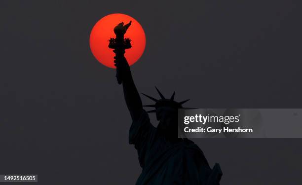 The sun is shrouded as it sets behind the Statue of Liberty in a hazy sky caused by smoke drifting into the Northeast of the U.S. From wildfires in...