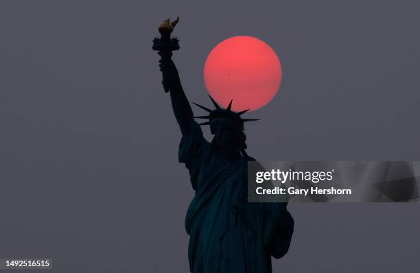 The sun is shrouded as it sets behind the Statue of Liberty in a hazy sky caused by smoke drifting into the Northeast of the U.S. From wildfires in...