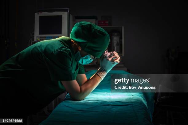 healthcare worker in surgical gown praying for god's blessings to patient after surgery in operating room. - nurse meditating stock pictures, royalty-free photos & images