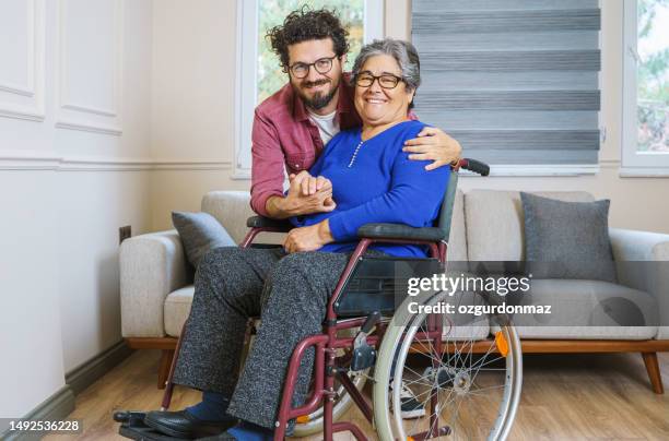 mid adult man hugging his disabled mother at home - wheelchair stock pictures, royalty-free photos & images