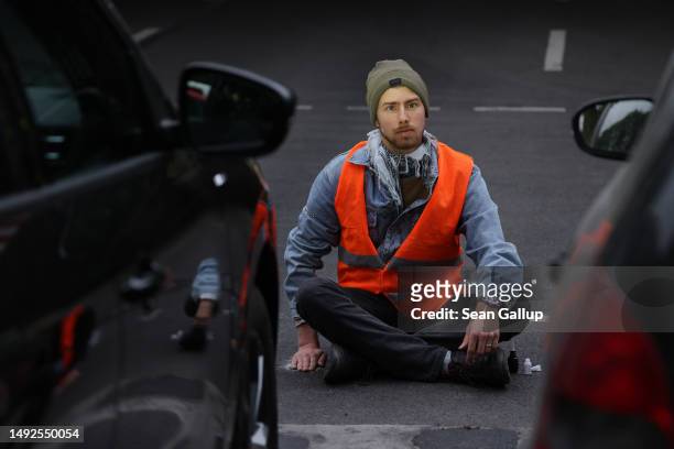 An activist of the Last Generation climate action group sits with one hand glued to the asphalt as he and others blocked Puschkinallee avenue on May...