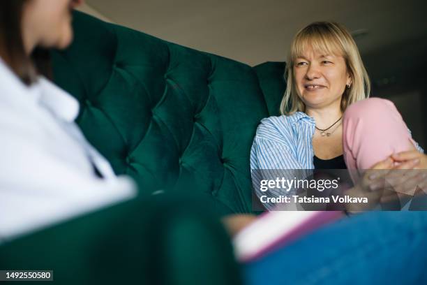 low angle view of two middle-aged women sitting on couch talking during therapy session - two women talking stockfoto's en -beelden