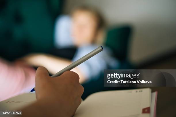 hand of unrecognizable woman holding pen and notebook with blurred woman lying on sofa in background - psychiatrists couch fotografías e imágenes de stock