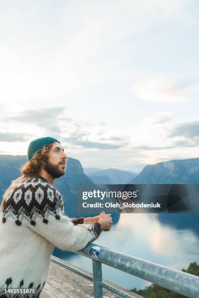 man in knitted sweater looking at scenic view of aurlandsfjord in norway from stegastein viewpoint - fashion range stock pictures, royalty-free photos & images