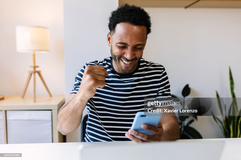 Excited young african american man winning on internet lottery betting online on smartphone app. Millennial guy celebrating victory enjoying success sports bet on cellphone.