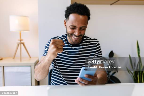 excited young african american man winning on internet lottery betting online on smartphone app. millennial guy celebrating victory enjoying success sports bet on cellphone. - gambling - fotografias e filmes do acervo