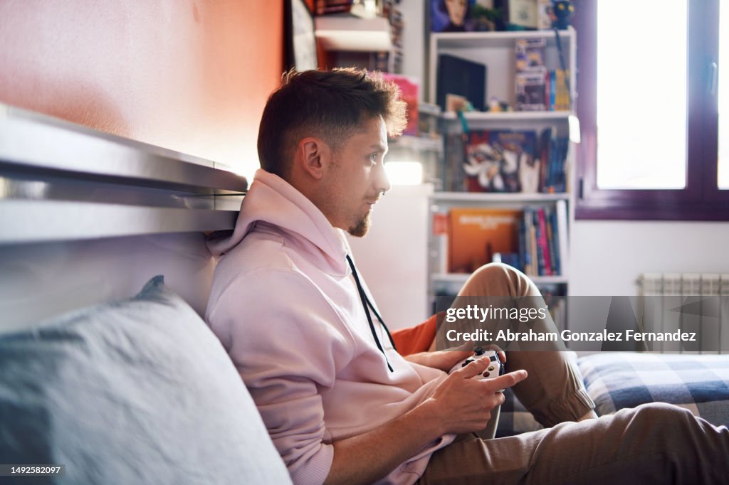 Profile of a happy man sitting on a bed playing console