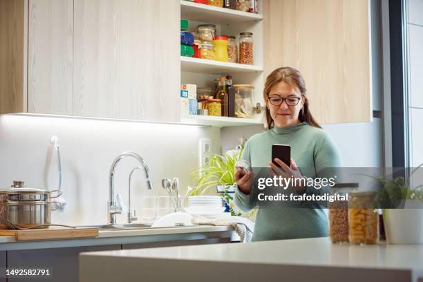 donna in cucina che usa il telefono e tenendo il cibo in scatola - dispensa foto e immagini stock