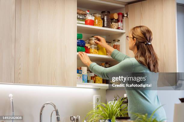 femme cueillant un pot d’ingrédients dans la cuisine du placard - placard photos et images de collection