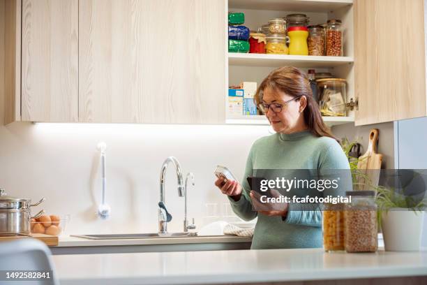 la donna in cucina controlla la data di scadenza dei prodotti in scatola - dispensa foto e immagini stock