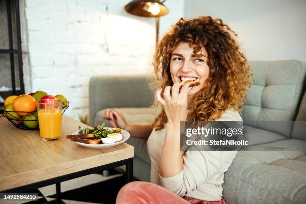 woman is having breakfast in the living room - eating bread stock pictures, royalty-free photos & images