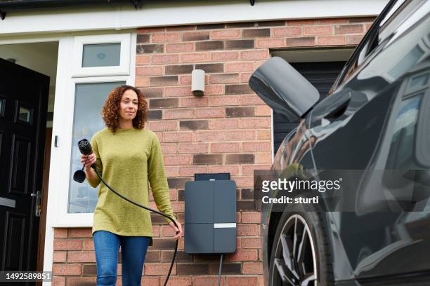 homeowner charging electric car on driveway - opladen stockfoto's en -beelden