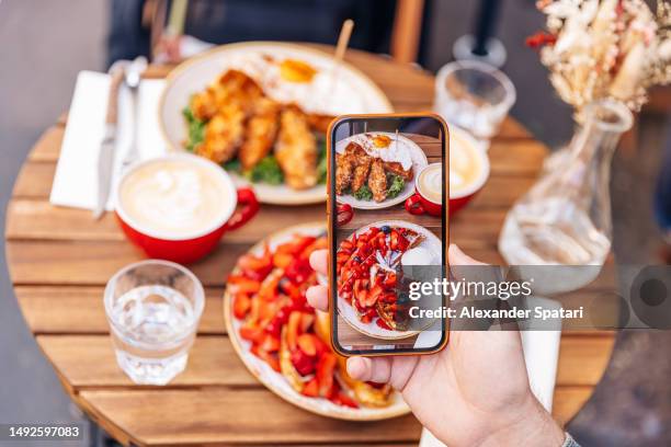 man photographing his breakfast at the cafe using smartphone, personal perspective view - foodie stockfoto's en -beelden