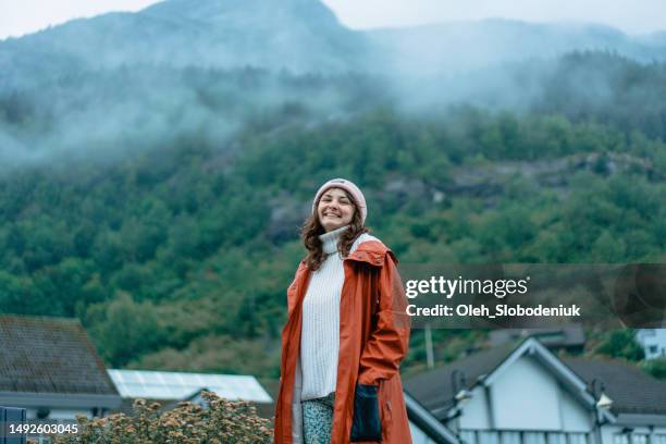woman in raincoat standing on the background of odda town and fjord during the rain - traditionally norwegian stockfoto's en -beelden