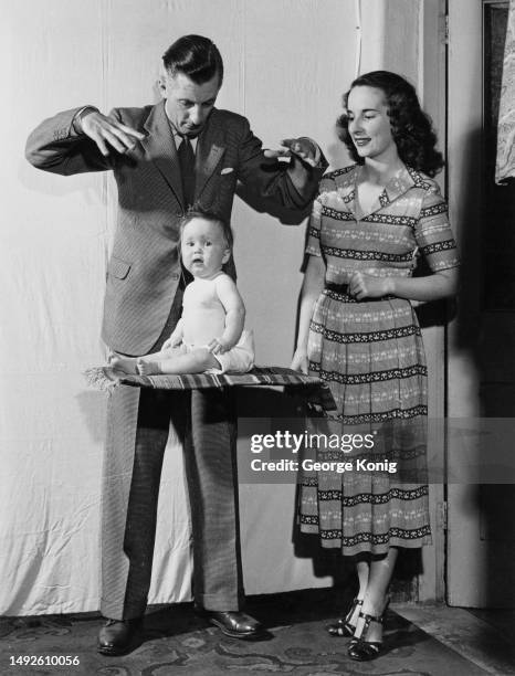 Magician Jon Evans levitates his baby daughter, Kim, on a magic carpet watched by his partner, location unspecified, United Kingdom, circa 1952.