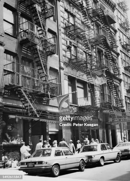 Pedestrians passing cars parked alongside the sidewalk beneath the fire escapes up the side of a building in the Greenwich Village neighbourhood in...