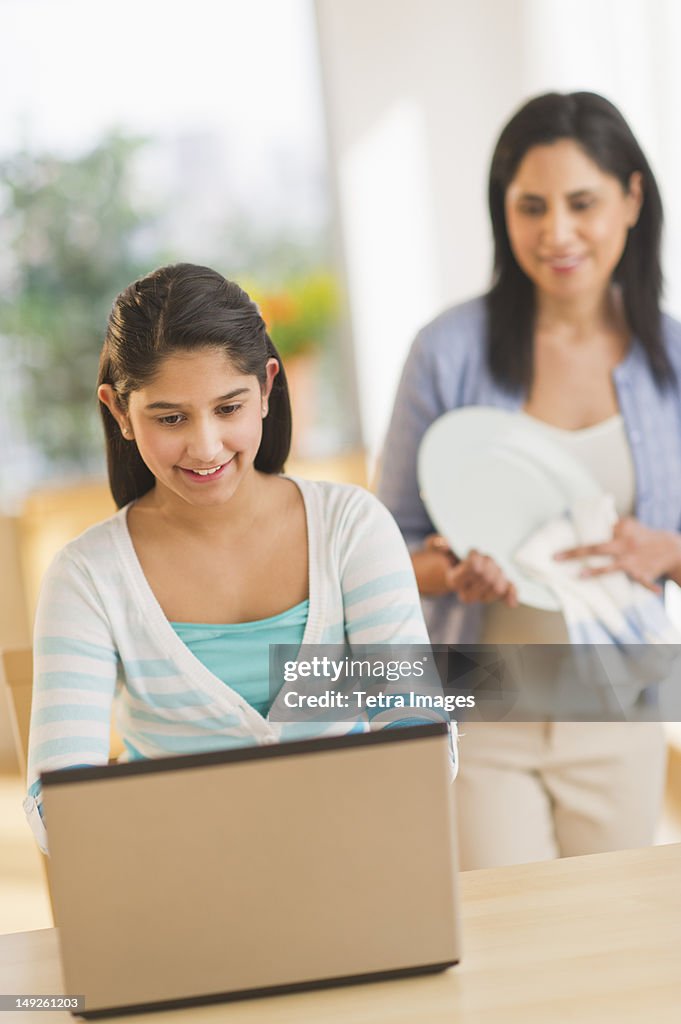 USA, New Jersey, Jersey City, Girl using laptop (12-13) at home, mother in background