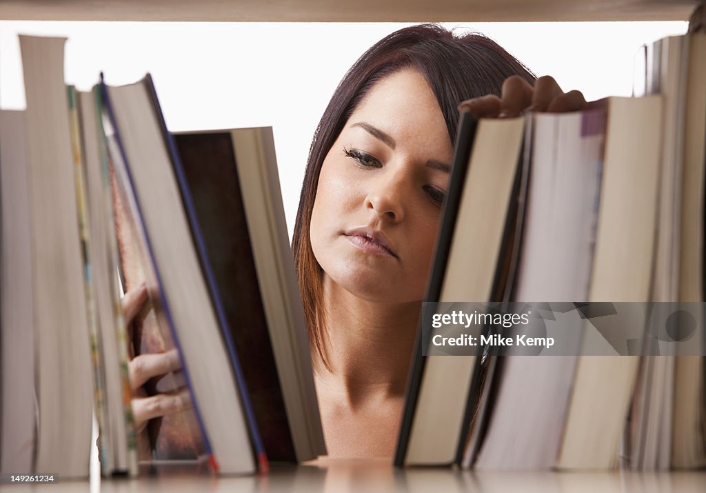 Portrait of young woman searching book on shelf