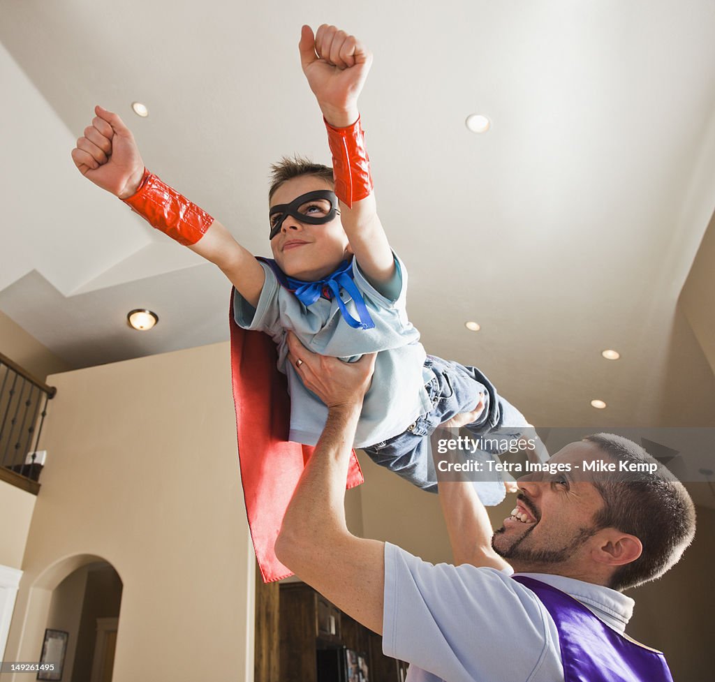 Father holding aloft his son (8-9) dressed up in fancy dress costume