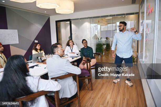 mid-adult man with a prosthetic leg presenting to his colleagues in a meeting room - disabilitycollection ストックフォトと画像