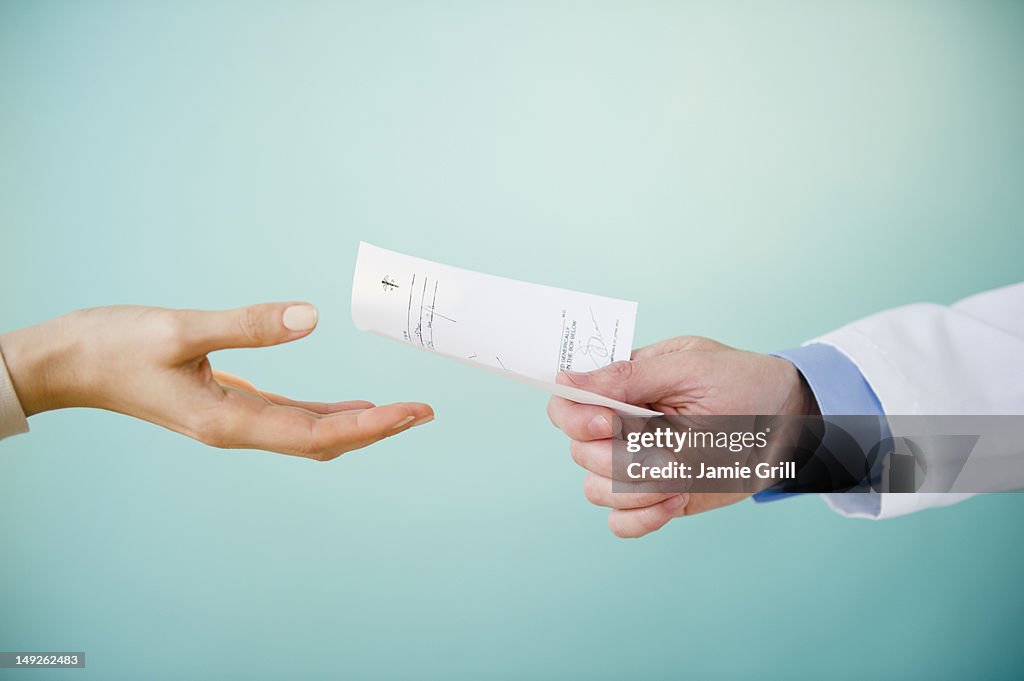 Close up of doctor's hand giving prescription to patient, studio shot