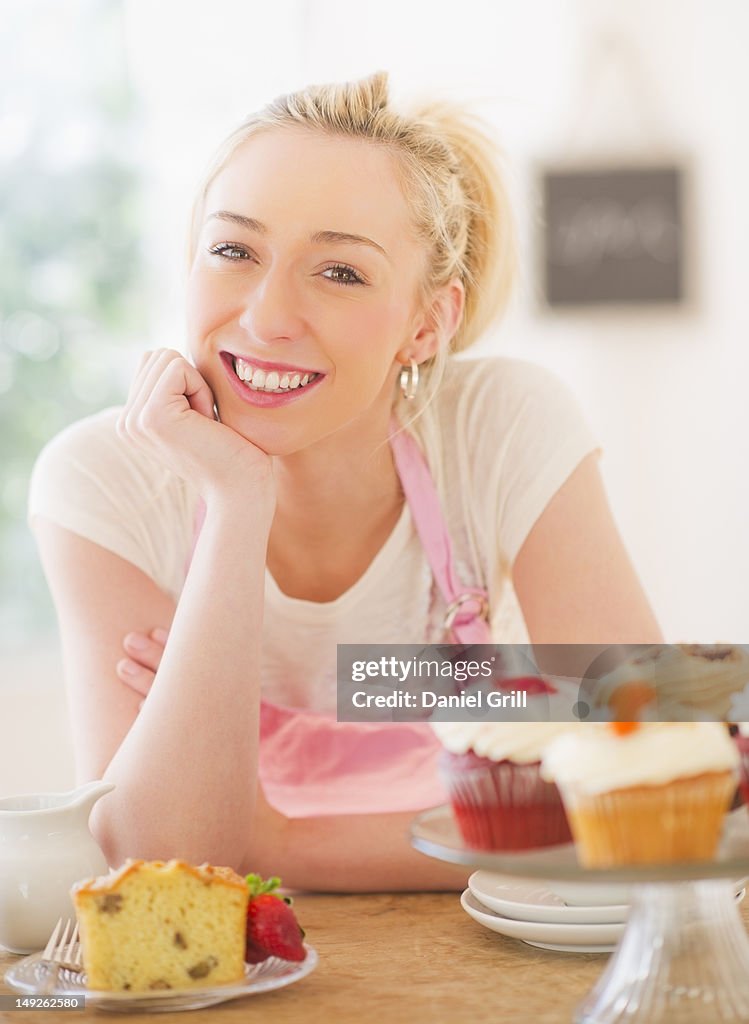 USA, New Jersey, Jersey City, Smiling young woman in apron leaning on table with cakes