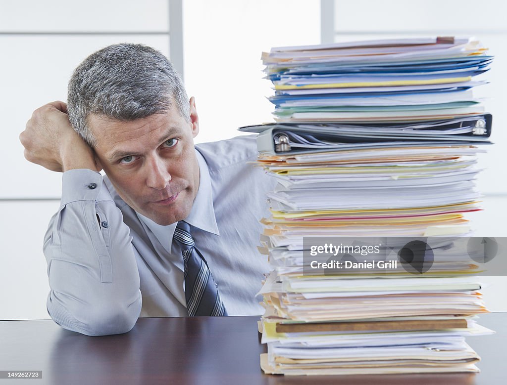 Businessman sitting next to large stack of documents