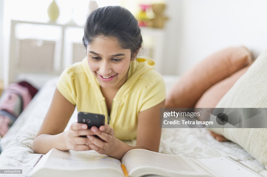 USA, New Jersey, Jersey City, Girl (12-13) lying on bed and texting