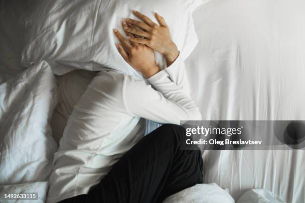 woman crying in bed and hiding face under pillow. panic attack or unstable psyche - psyche stock pictures, royalty-free photos & images