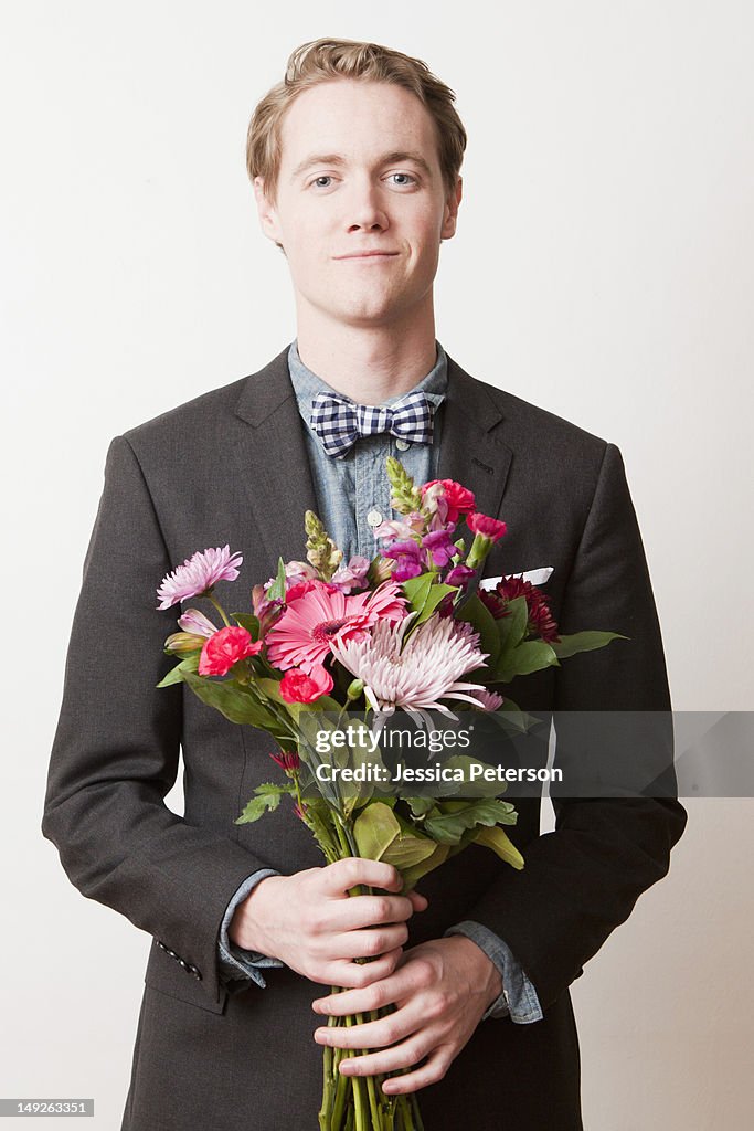 Portrait of young handsome man holding bunch of flowers