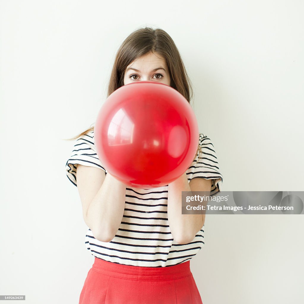 Studio shot of young woman blowing balloon