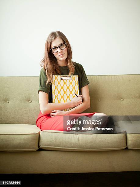 young woman sitting on sofa with clipboard - fersensitz stock-fotos und bilder