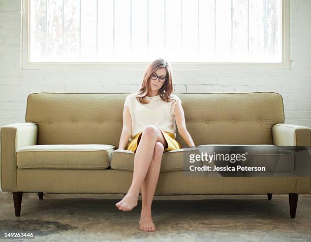 young woman sitting on sofa - legs crossed at knee stock pictures, royalty-free photos & images