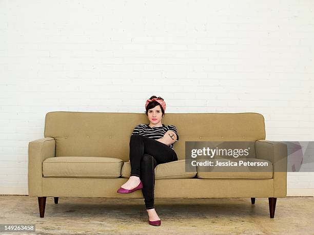 young woman sitting on sofa - überkreuzte beine stock-fotos und bilder