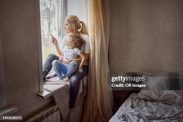 mother sitting with little daughter on windowsill at home - tochter zeigt stock-fotos und bilder