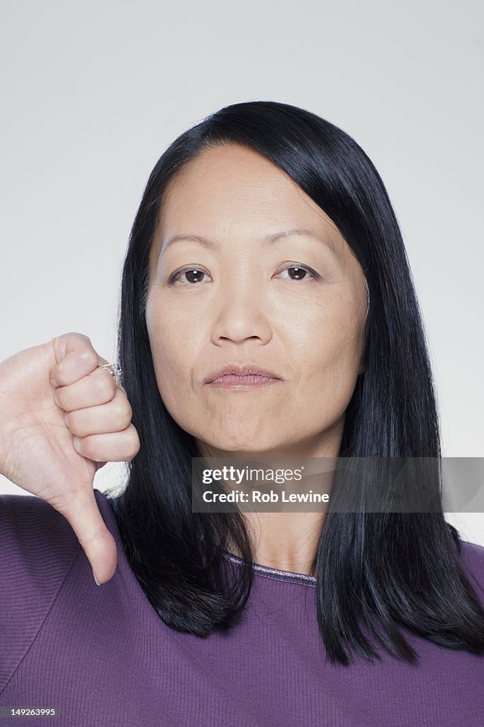 Studio portrait of mature woman showing thumbs down sign