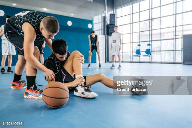 teenage boy injuring his ankle while playing basketball indoors - 四肢 個照片及圖片檔