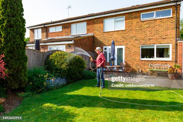 man watering his garden with a hose in summer - garden hose stock pictures, royalty-free photos & images