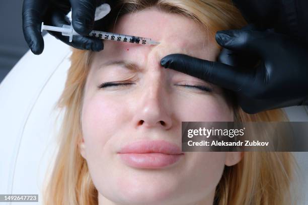 a beautiful young woman, a client in the cosmetologist's office. a health worker gives anti-aging botox injections at a beauty center. the concept of modern cosmetic procedures. smoothing facial wrinkles on the face. plasmolifting and plasma therapy. - anti age stock-fotos und bilder