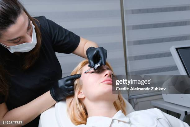 a beautiful young woman, a client in the cosmetologist's office. a health worker gives anti-aging botox injections at a beauty center. the concept of modern cosmetic procedures. smoothing facial wrinkles on the face. plasmolifting and plasma therapy. - anti age stock-fotos und bilder