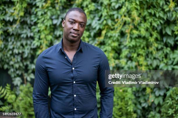 man looking at camera while standing in a garden - groen shirt stockfoto's en -beelden