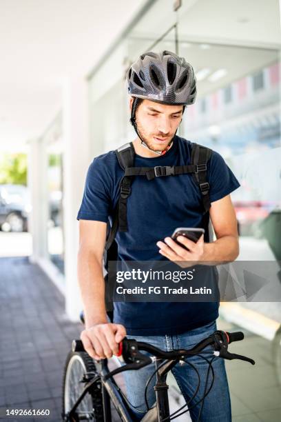junger fahrradlieferant, der mobiltelefon im freien verwendet - navigationsinstrument stock-fotos und bilder