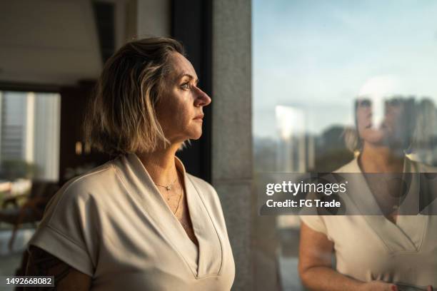 contemplative mature woman looking through the window - door het raam kijken stockfoto's en -beelden