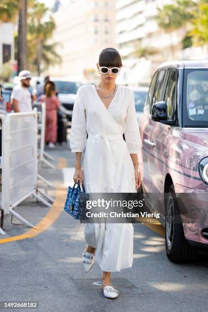 Katya Tolstova wears white dress, blue MCM bag, slippers, sunglasses during the 76th Cannes film festival on May 23, 2023 in Cannes, France.