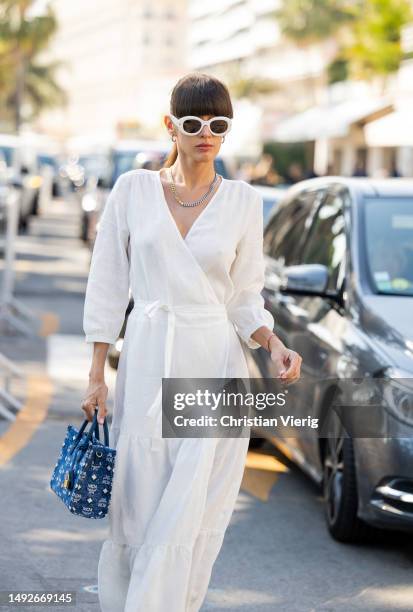 Katya Tolstova wears white dress, blue MCM bag, slippers, sunglasses during the 76th Cannes film festival on May 23, 2023 in Cannes, France.